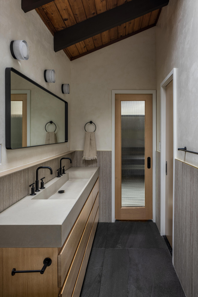 This is an example of a small contemporary master bathroom in New York with flat-panel cabinets, light wood cabinets, an open shower, a one-piece toilet, beige walls, slate floors, an integrated sink, concrete benchtops, black floor, a shower curtain, grey benchtops, a double vanity, exposed beam and a floating vanity.