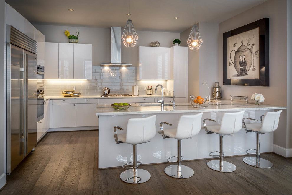 Inspiration for a large modern l-shaped eat-in kitchen in Houston with an undermount sink, flat-panel cabinets, white cabinets, quartzite benchtops, white splashback, ceramic splashback, stainless steel appliances, light hardwood floors and grey floor.