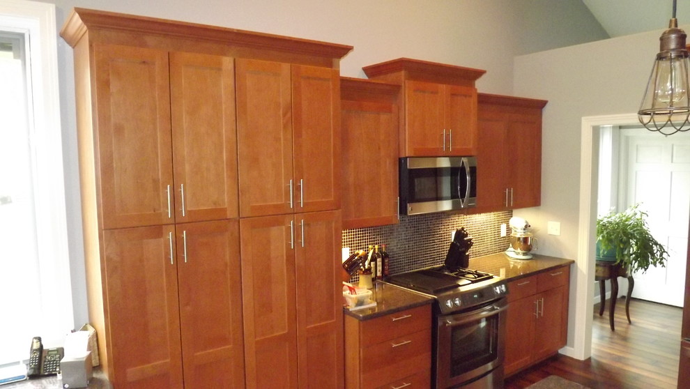 Transitional u-shaped medium tone wood floor open concept kitchen photo with an undermount sink, flat-panel cabinets, medium tone wood cabinets, granite countertops, black backsplash, glass tile backsplash, stainless steel appliances and a peninsula