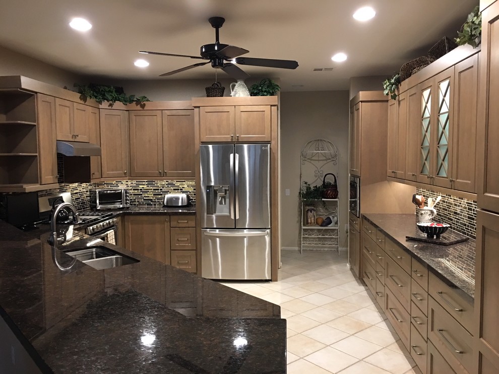 This is an example of a mid-sized transitional open plan kitchen in Phoenix with an undermount sink, shaker cabinets, light wood cabinets, granite benchtops, multi-coloured splashback, glass tile splashback, stainless steel appliances, porcelain floors, a peninsula, beige floor and black benchtop.