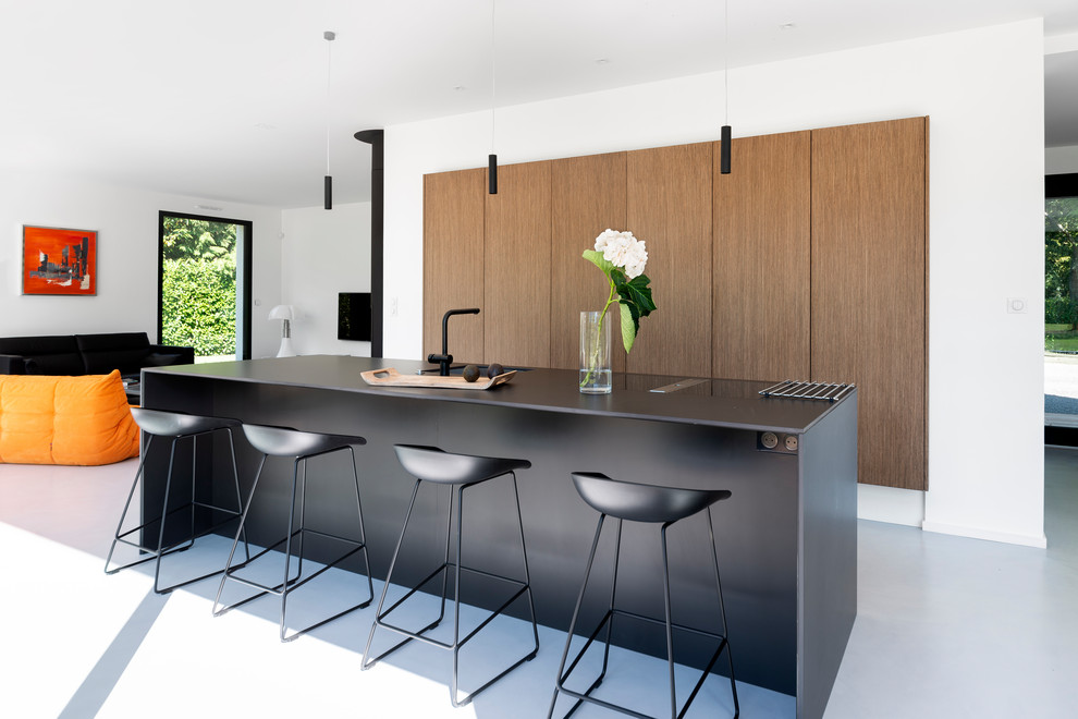 This is an example of a large contemporary galley eat-in kitchen in Nantes with an undermount sink, flat-panel cabinets, light wood cabinets, concrete floors, with island, grey floor and black benchtop.