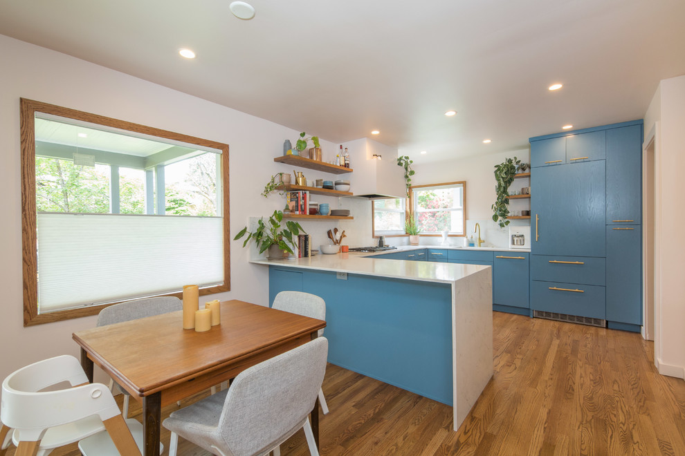 Inspiration for a midcentury u-shaped eat-in kitchen in Portland with flat-panel cabinets, blue cabinets, white splashback, panelled appliances, medium hardwood floors, a peninsula and white benchtop.