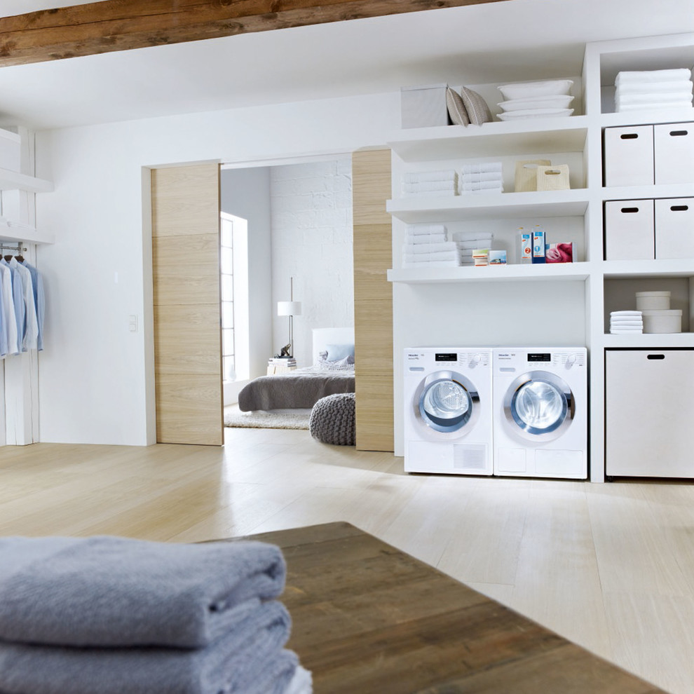 Photo of a large contemporary single-wall dedicated laundry room in Oxfordshire with white cabinets, white walls, light hardwood floors and a side-by-side washer and dryer.