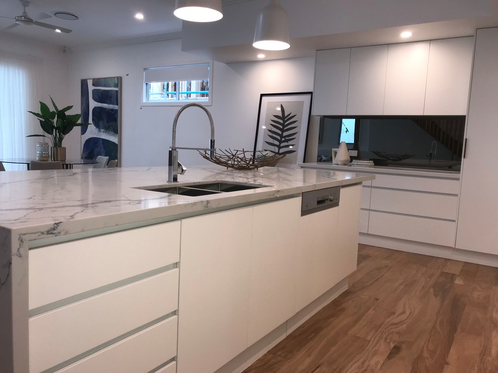 This is an example of a large contemporary galley kitchen in Brisbane with granite benchtops, black splashback, glass sheet splashback, stainless steel appliances and light hardwood floors.
