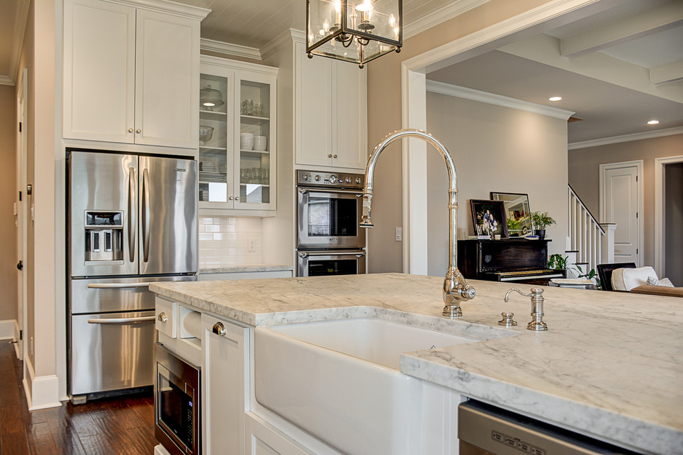 This is an example of a mid-sized traditional l-shaped eat-in kitchen in Austin with a farmhouse sink, shaker cabinets, white cabinets, marble benchtops, white splashback, subway tile splashback, stainless steel appliances, medium hardwood floors and with island.
