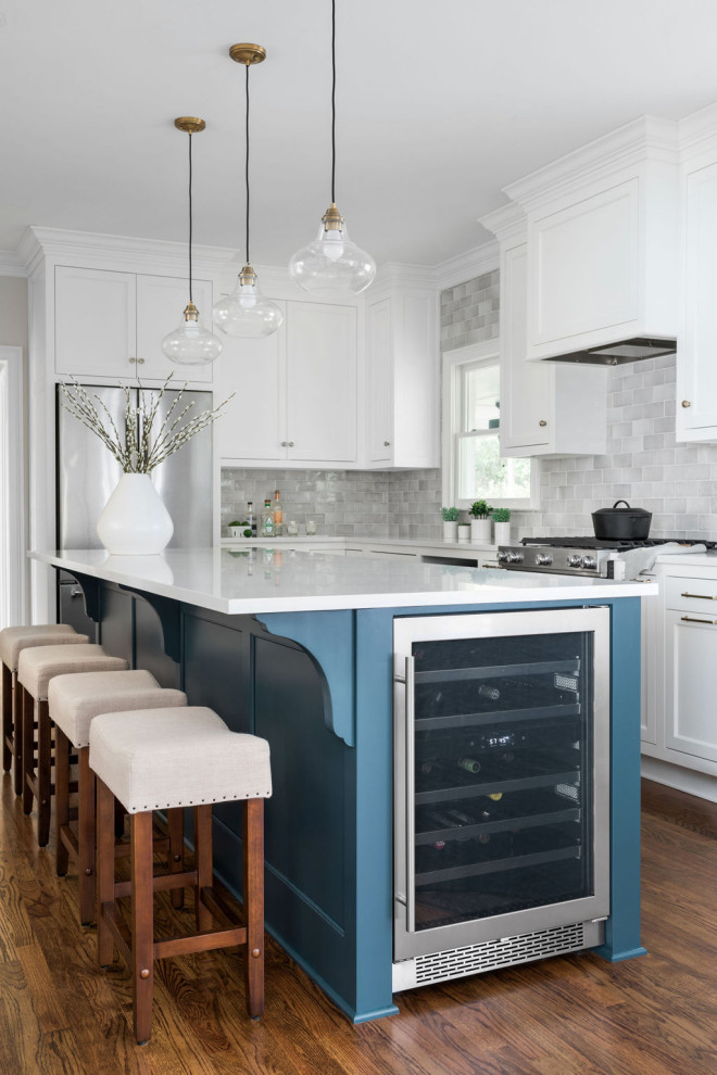 Inspiration for a mid-sized transitional galley kitchen in Atlanta with an undermount sink, recessed-panel cabinets, white cabinets, quartz benchtops, grey splashback, porcelain splashback, stainless steel appliances, medium hardwood floors, with island, brown floor and white benchtop.