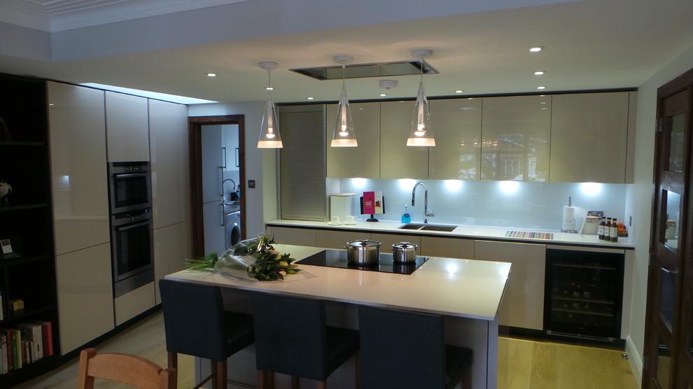 Large contemporary u-shaped eat-in kitchen in London with a double-bowl sink, raised-panel cabinets, white cabinets, granite benchtops, grey splashback, porcelain splashback, stainless steel appliances, light hardwood floors and with island.