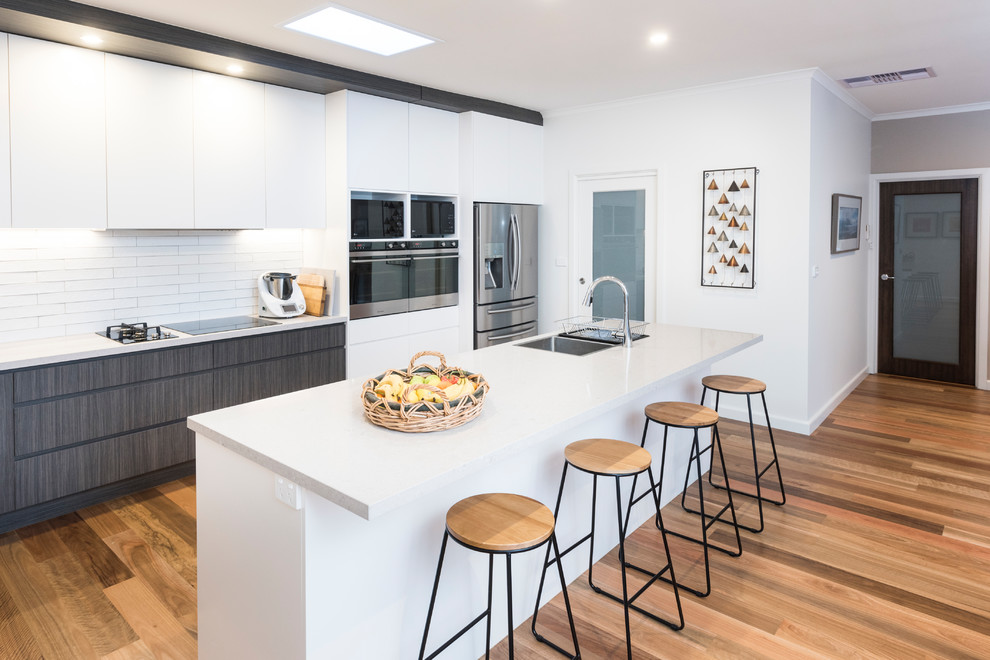 Design ideas for an eclectic single-wall eat-in kitchen in Melbourne with an undermount sink, flat-panel cabinets, white cabinets, granite benchtops, white splashback, subway tile splashback, white appliances, medium hardwood floors and with island.