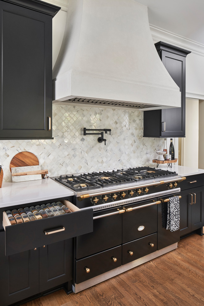 This is an example of a mid-sized contemporary l-shaped eat-in kitchen in Charlotte with a farmhouse sink, recessed-panel cabinets, black cabinets, quartz benchtops, white splashback, marble splashback, black appliances, medium hardwood floors, with island, brown floor and white benchtop.