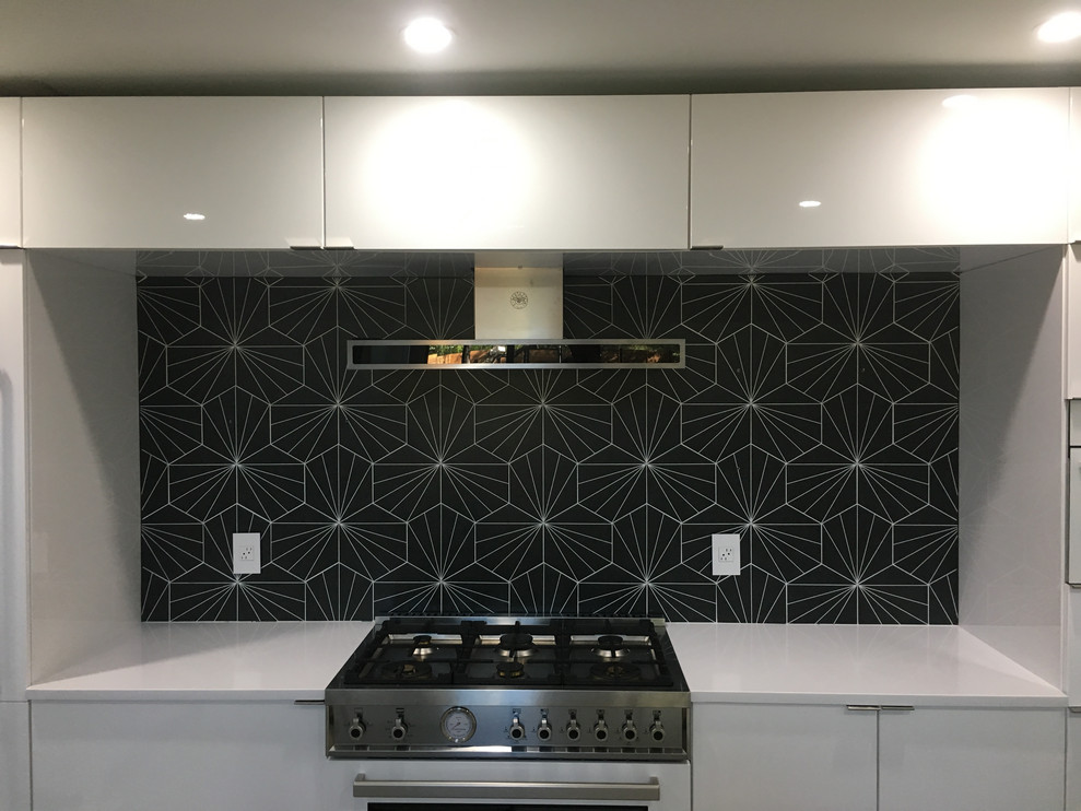 Mid-sized modern single-wall open plan kitchen in Austin with an undermount sink, flat-panel cabinets, white cabinets, quartz benchtops, black splashback, porcelain splashback, white appliances, concrete floors, with island, grey floor and white benchtop.