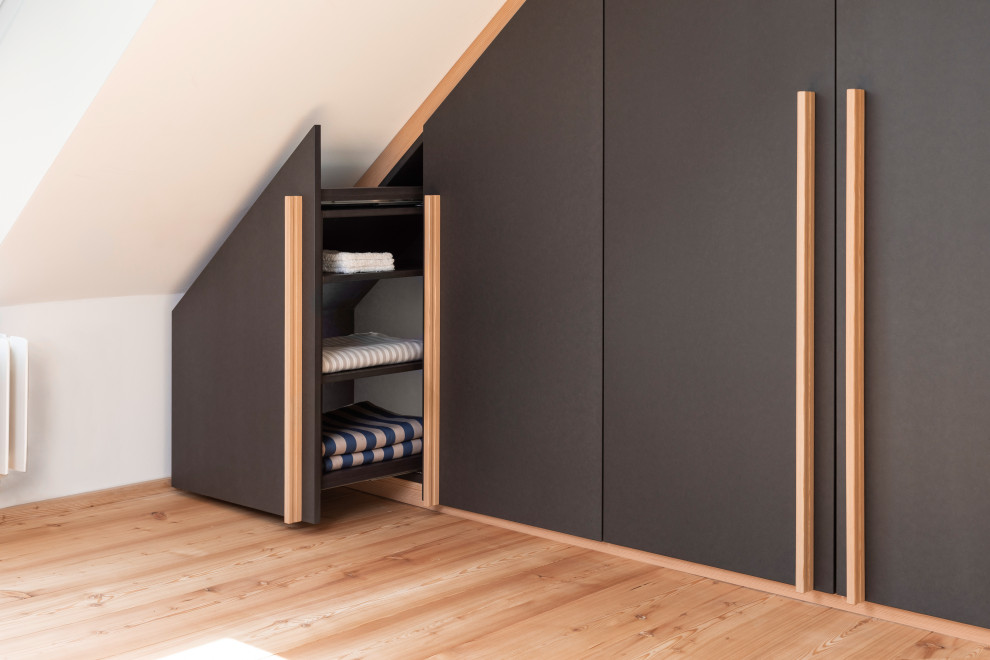 This is an example of a mid-sized modern gender-neutral walk-in wardrobe in Stuttgart with flat-panel cabinets, black cabinets, light hardwood floors, brown floor and exposed beam.