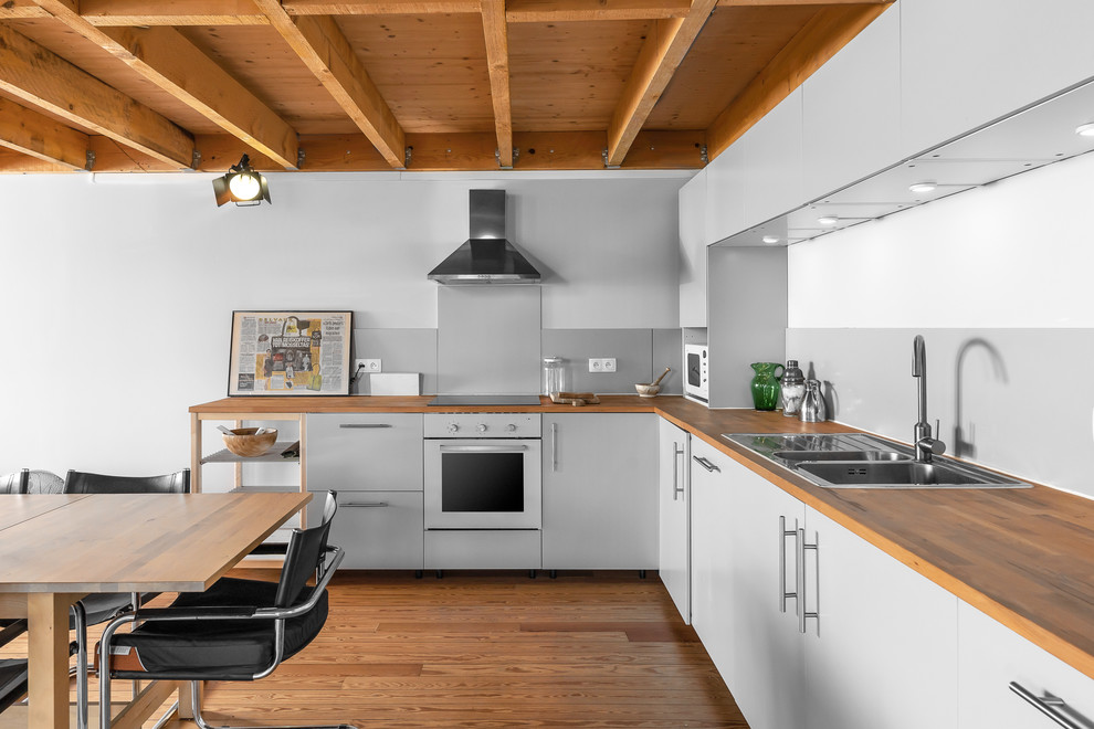 Industrial l-shaped eat-in kitchen in Nice with wood benchtops, medium hardwood floors, no island, a double-bowl sink, flat-panel cabinets, grey cabinets, brown floor and brown benchtop.