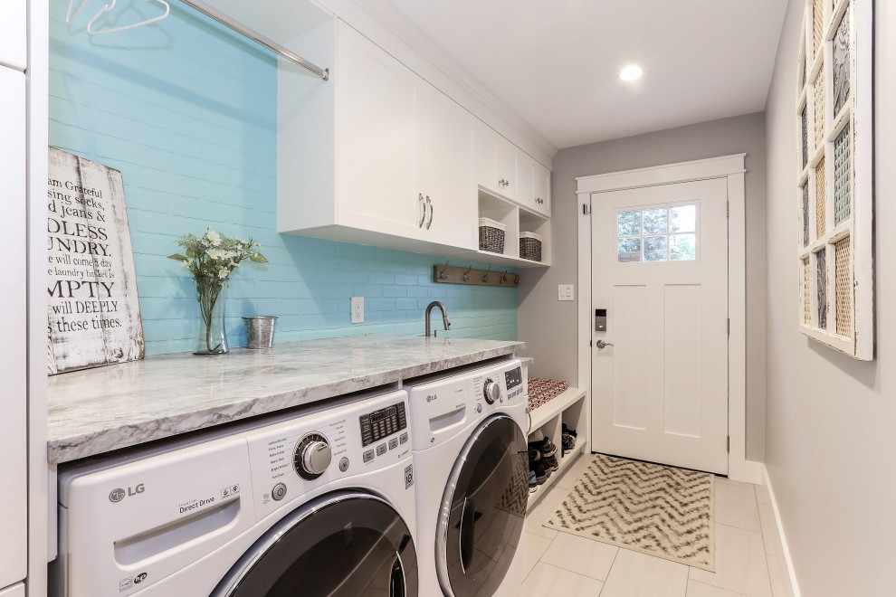 Transitional single-wall laundry room in Other with recessed-panel cabinets, white cabinets, blue walls, brick floors, a side-by-side washer and dryer, grey floor and grey benchtop.
