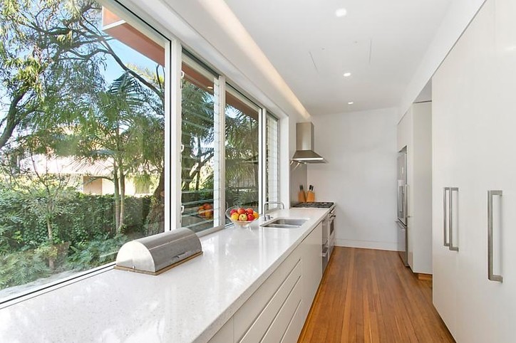 This is an example of a mid-sized beach style galley eat-in kitchen in Sydney with a double-bowl sink, granite benchtops, metallic splashback, stainless steel appliances, medium hardwood floors and no island.