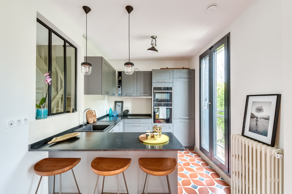 Photo of a contemporary u-shaped separate kitchen in Paris with a drop-in sink, shaker cabinets, grey cabinets, white splashback, mosaic tile splashback, black appliances, cement tiles, a peninsula and multi-coloured floor.