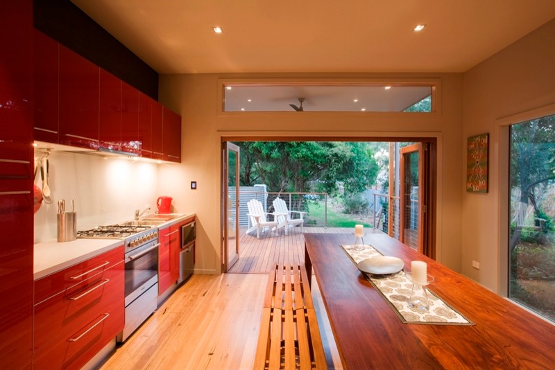 Photo of a mid-sized beach style single-wall eat-in kitchen in Melbourne with a double-bowl sink, beaded inset cabinets, red cabinets, terrazzo benchtops, white splashback, ceramic splashback, stainless steel appliances, light hardwood floors and no island.