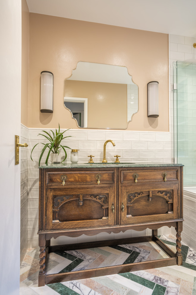 This is an example of a small traditional kids bathroom in London with brown cabinets, a drop-in tub, a shower/bathtub combo, white tile, ceramic tile, porcelain floors, a drop-in sink, marble benchtops, multi-coloured floor, green benchtops, a single vanity, a freestanding vanity and recessed-panel cabinets.