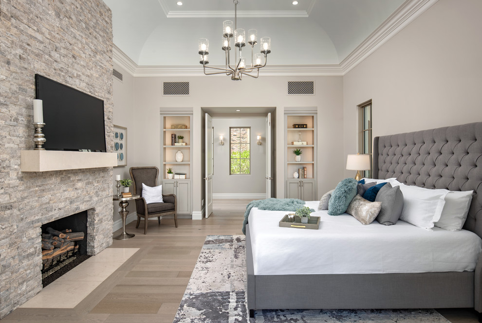 Inspiration for a transitional master bedroom in Phoenix with beige walls, light hardwood floors, a standard fireplace, a stone fireplace surround and beige floor.