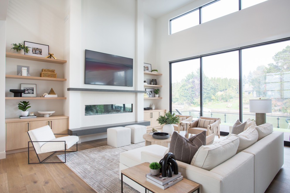 Diseño de sala de estar abierta minimalista grande con paredes blancas, suelo de madera en tonos medios, todas las chimeneas, marco de chimenea de yeso, televisor colgado en la pared y suelo marrón