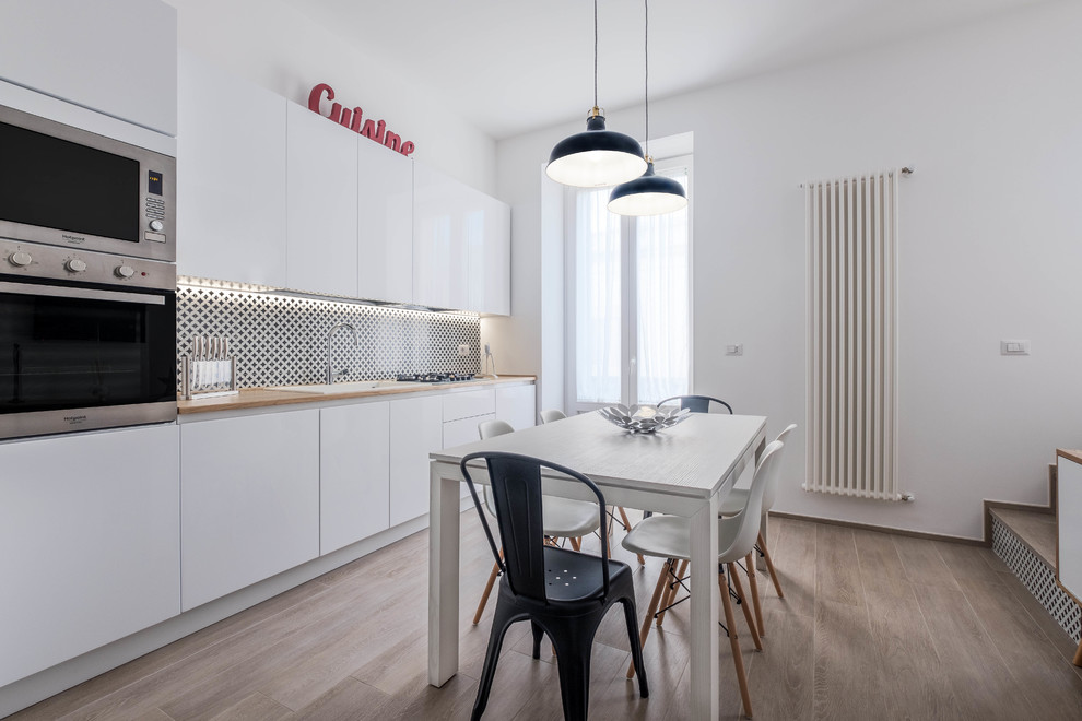 Photo of a mid-sized contemporary single-wall eat-in kitchen in Bari with a single-bowl sink, flat-panel cabinets, white cabinets, wood benchtops, multi-coloured splashback, stainless steel appliances, no island and light hardwood floors.