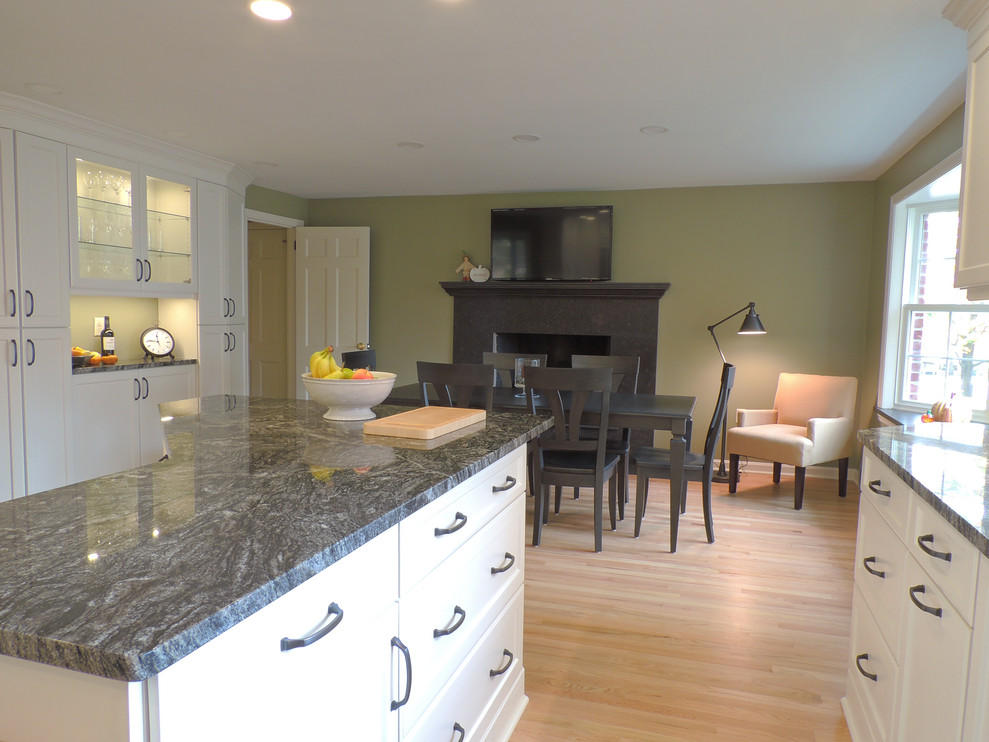 Kitchen - transitional light wood floor kitchen idea with a single-bowl sink, shaker cabinets, white cabinets, granite countertops, white backsplash, ceramic backsplash, stainless steel appliances, an island and black countertops