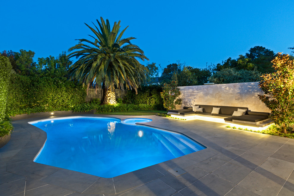Contemporary backyard custom-shaped pool in Melbourne with natural stone pavers and a hot tub.