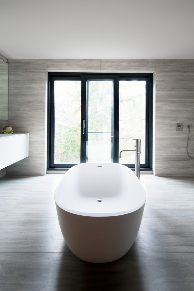 Photo of a mid-sized modern bathroom in Hamburg with flat-panel cabinets, white cabinets, a freestanding tub, beige tile and beige floor.