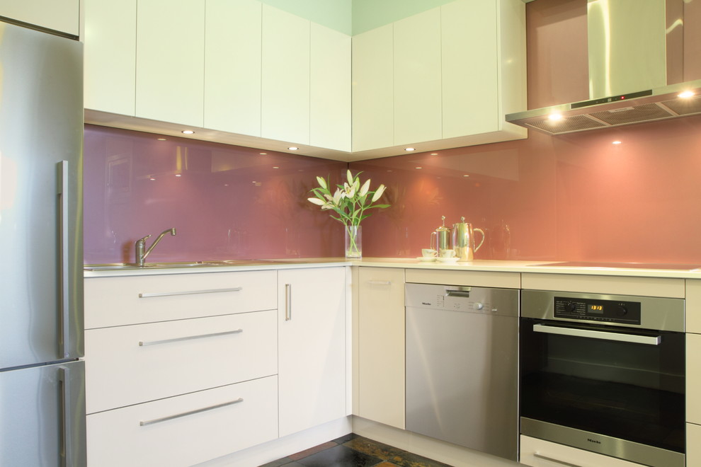 Mid-sized contemporary u-shaped separate kitchen in Sydney with a double-bowl sink, flat-panel cabinets, white cabinets, quartz benchtops, pink splashback, glass sheet splashback, stainless steel appliances and terra-cotta floors.