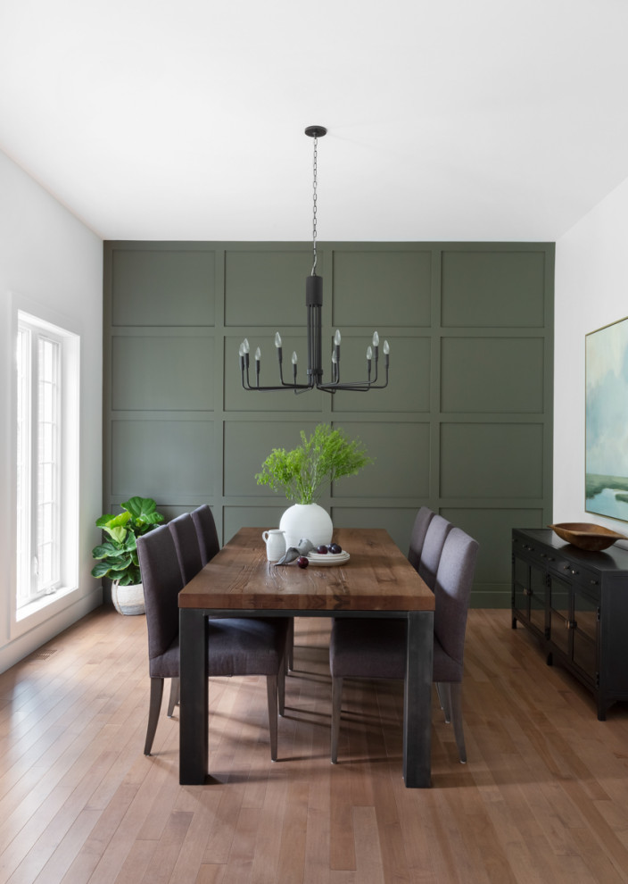 This is an example of a large transitional separate dining room in Montreal with green walls, medium hardwood floors, no fireplace, brown floor and panelled walls.