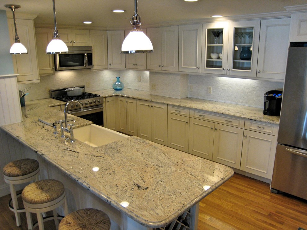 Open concept kitchen - mid-sized transitional u-shaped medium tone wood floor and brown floor open concept kitchen idea in Providence with a farmhouse sink, recessed-panel cabinets, white cabinets, granite countertops, white backsplash, ceramic backsplash, stainless steel appliances, a peninsula and gray countertops