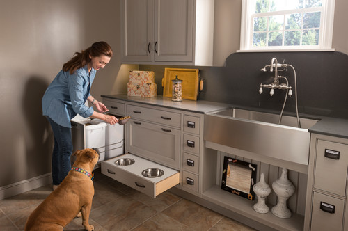 Woman using a pull-out dog feeding drawer built into a gray kitchen cabinet beside a farmhouse sink