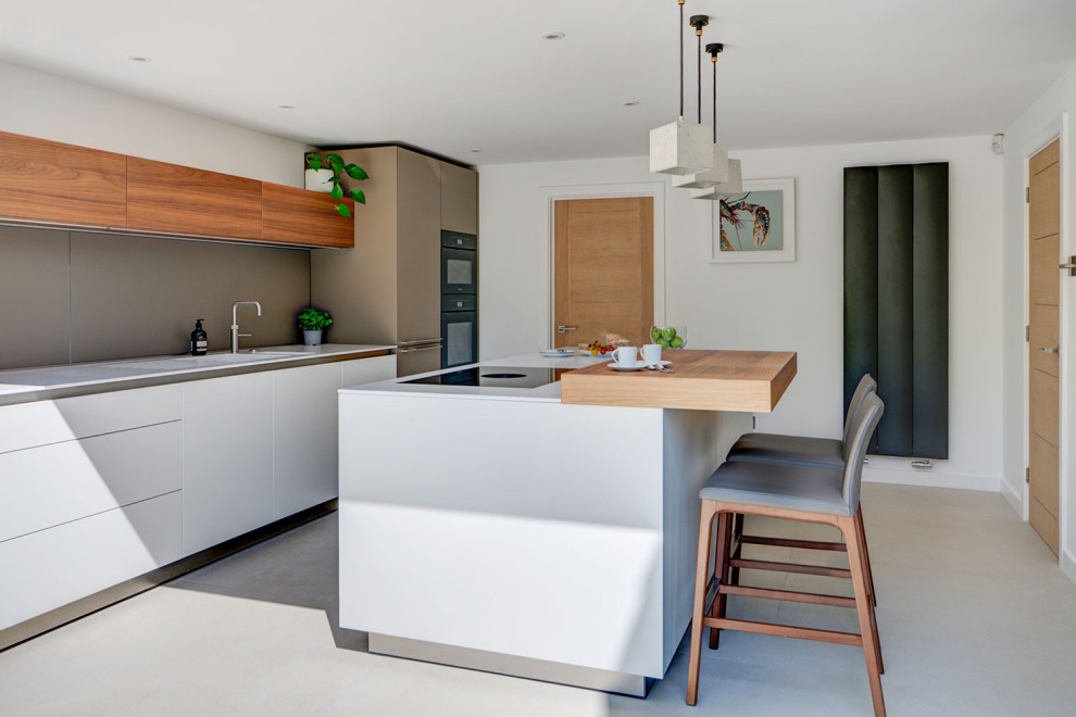 This is an example of a medium sized contemporary single-wall kitchen/diner in Wiltshire with an integrated sink, flat-panel cabinets, white cabinets, composite countertops, grey splashback, black appliances, porcelain flooring, an island and white worktops.