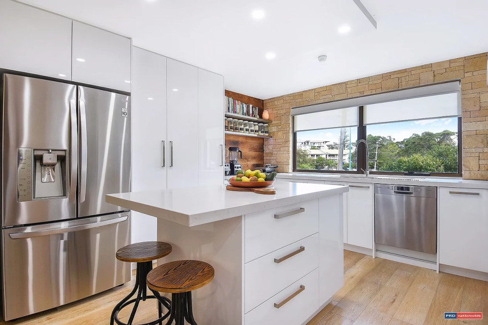 Inspiration for a large scandinavian u-shaped open plan kitchen in Gold Coast - Tweed with beaded inset cabinets, white cabinets, quartz benchtops, beige splashback, stone slab splashback, medium hardwood floors, with island, beige floor and white benchtop.