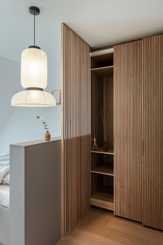 Medium sized world-inspired gender neutral dressing room in Munich with louvered cabinets, medium wood cabinets, light hardwood flooring and beige floors.