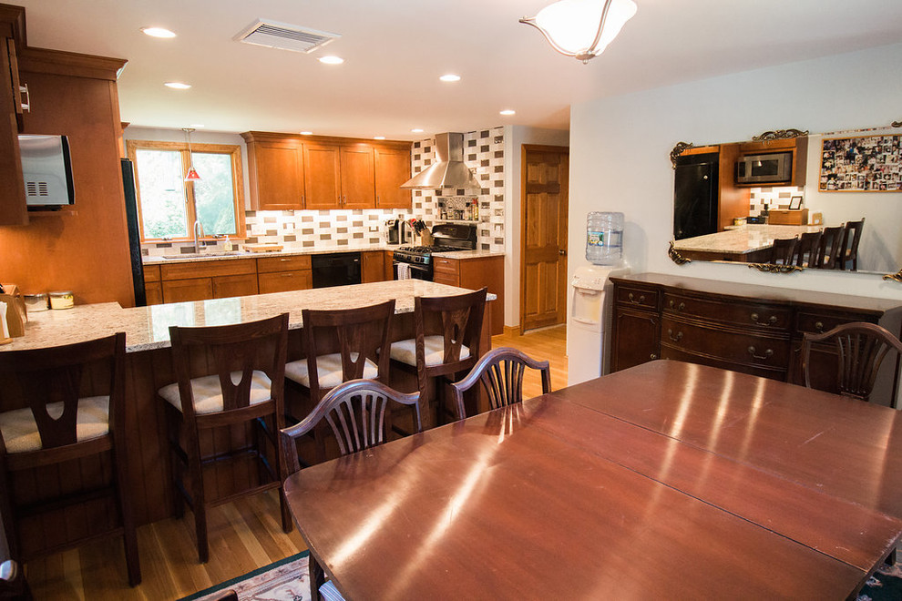 Mid-sized transitional u-shaped medium tone wood floor eat-in kitchen photo in Boston with an undermount sink, recessed-panel cabinets, medium tone wood cabinets, granite countertops, multicolored backsplash, subway tile backsplash, black appliances and a peninsula
