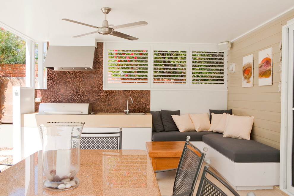 This is an example of a beach style backyard patio in Sydney with natural stone pavers and a roof extension.