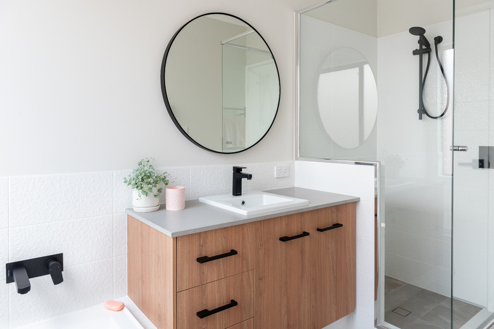 Photo of a contemporary kids bathroom in Perth with medium wood cabinets, a drop-in tub, white tile, ceramic tile, ceramic floors, a drop-in sink, engineered quartz benchtops, grey floor, a hinged shower door, grey benchtops, flat-panel cabinets, an alcove shower and white walls.