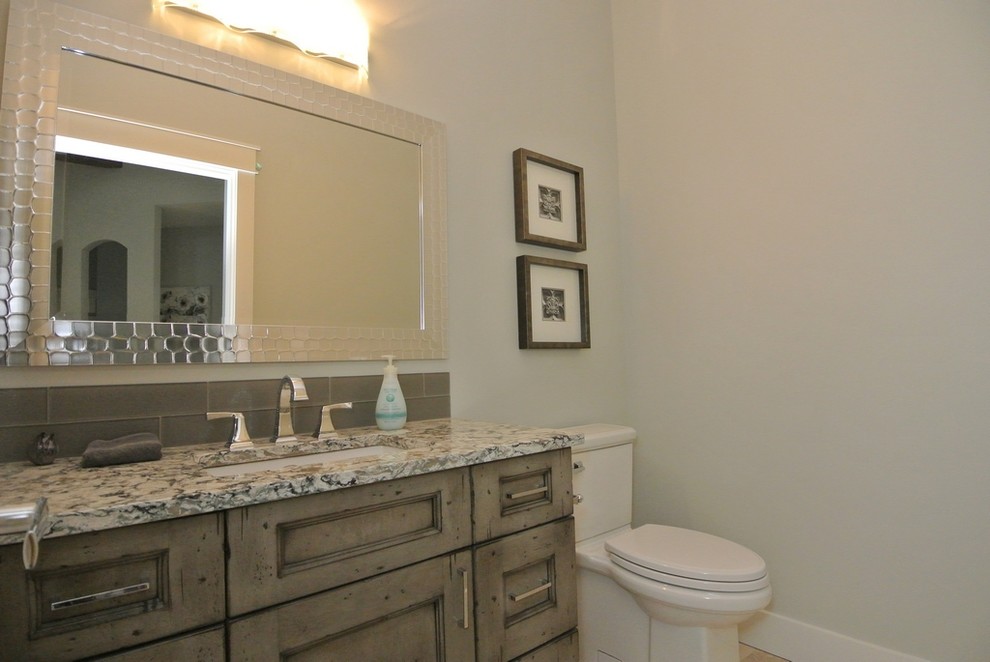 Photo of a small transitional powder room in Other with recessed-panel cabinets, distressed cabinets, a two-piece toilet, gray tile, ceramic tile, grey walls, ceramic floors, an undermount sink, quartzite benchtops, beige floor and grey benchtops.