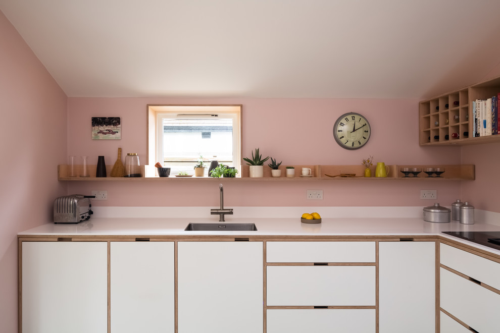 Scandinavian l-shaped kitchen in London with a single-bowl sink, flat-panel cabinets, white cabinets, pink splashback, white benchtop and solid surface benchtops.