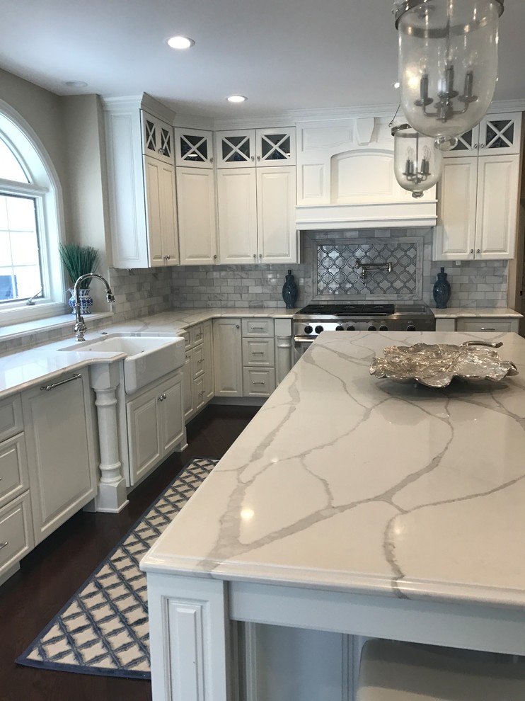 Dark wood floor kitchen photo with a farmhouse sink, raised-panel cabinets, white cabinets, quartz countertops, gray backsplash and marble backsplash