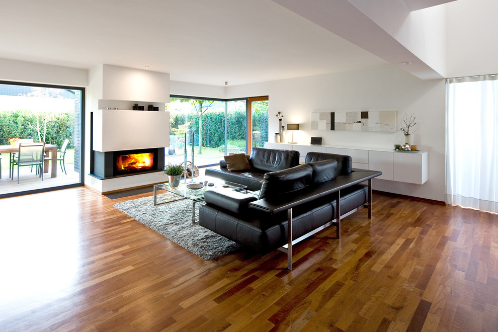 This is an example of a large contemporary formal open concept living room in Essen with white walls, medium hardwood floors, a standard fireplace, a metal fireplace surround and no tv.