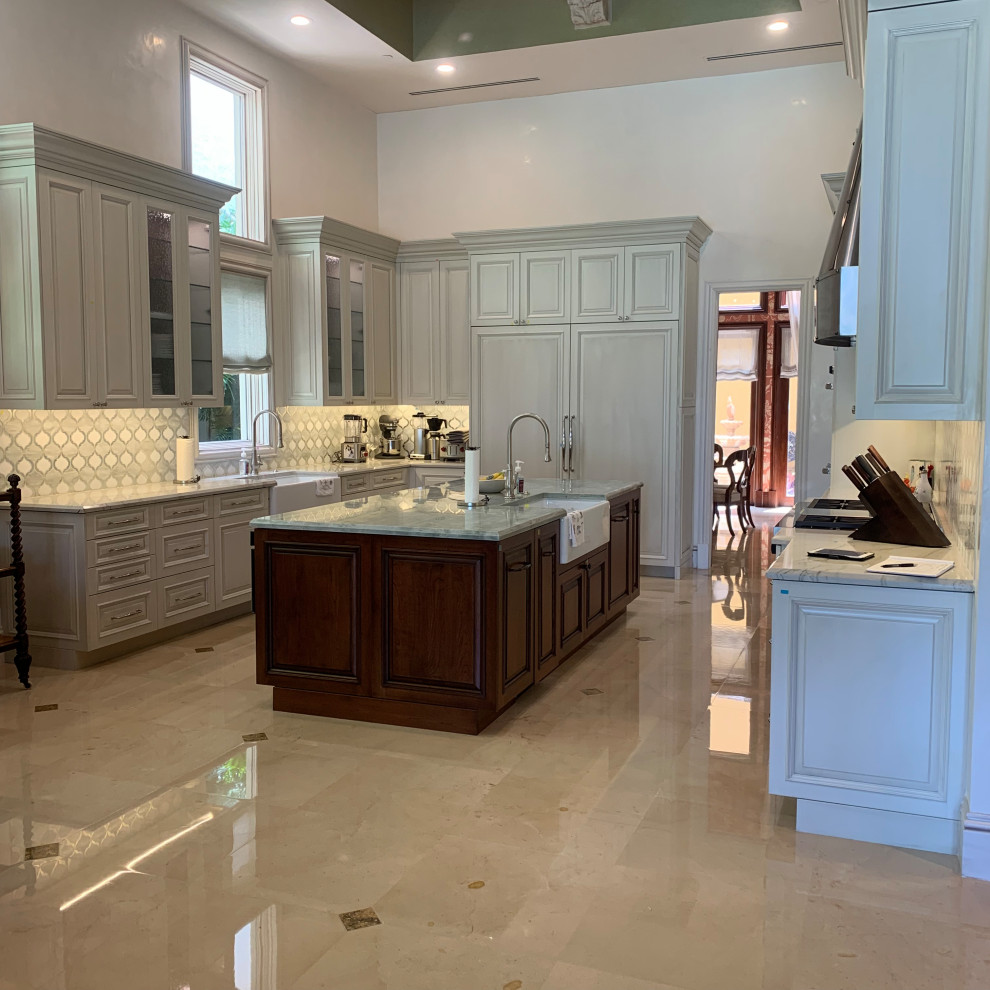 This is an example of a large transitional u-shaped kitchen in Miami with a farmhouse sink, raised-panel cabinets, white cabinets, quartzite benchtops, white splashback, mosaic tile splashback, panelled appliances, marble floors, with island, brown floor, green benchtop and coffered.