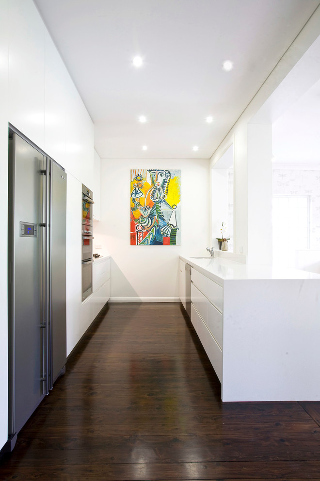 Design ideas for a contemporary u-shaped kitchen in Sydney with an undermount sink, flat-panel cabinets, white cabinets, quartz benchtops, glass sheet splashback and stainless steel appliances.