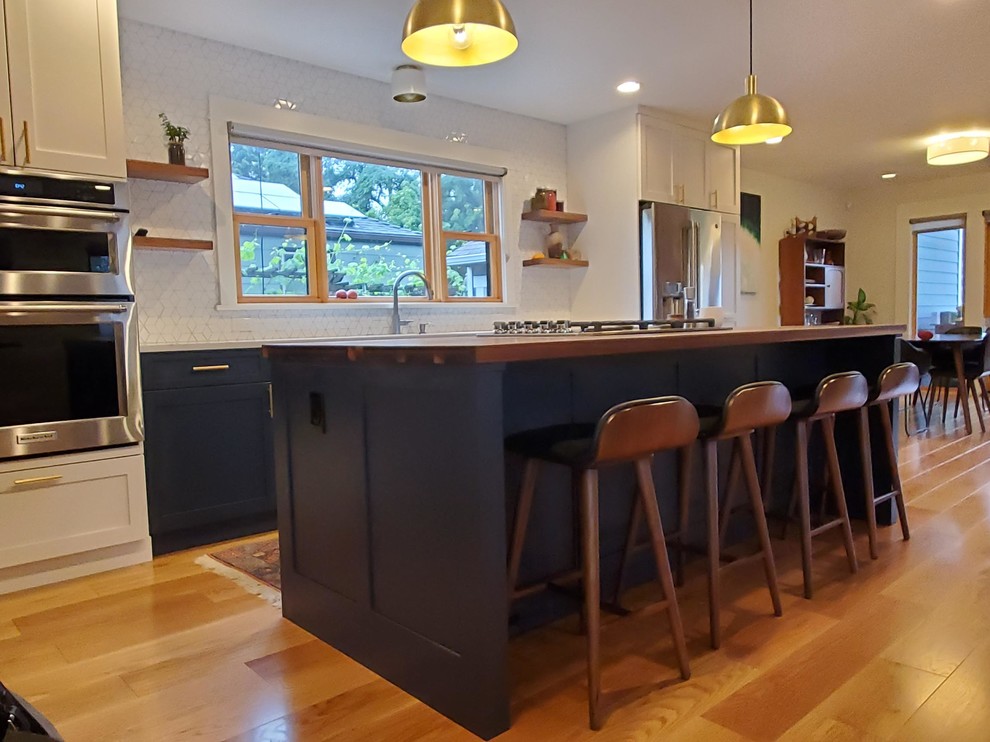 Photo of a mid-sized transitional single-wall eat-in kitchen in Seattle with an undermount sink, shaker cabinets, blue cabinets, wood benchtops, white splashback, porcelain splashback, stainless steel appliances, medium hardwood floors, with island and brown floor.