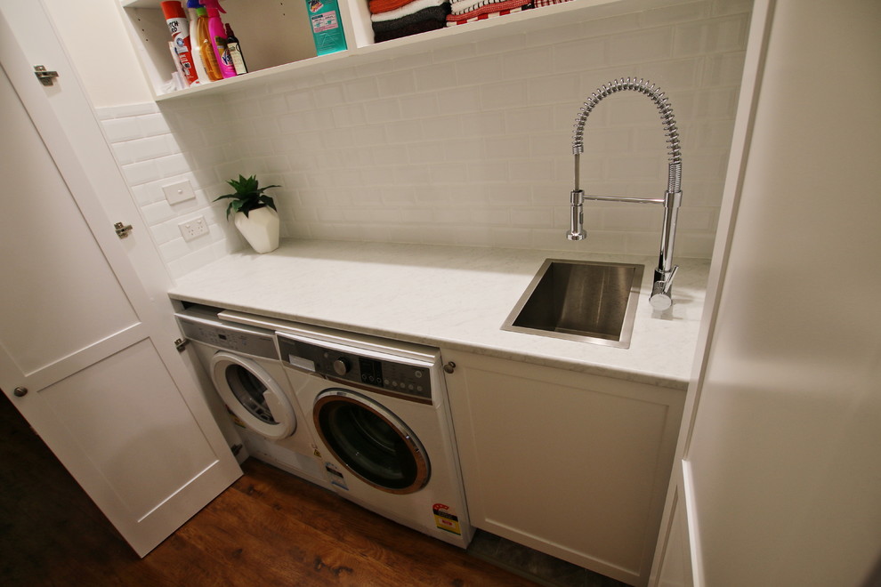 Design ideas for a small transitional single-wall dedicated laundry room in Sydney with a single-bowl sink, shaker cabinets, white cabinets, laminate benchtops, white walls, medium hardwood floors, a side-by-side washer and dryer, brown floor and white benchtop.