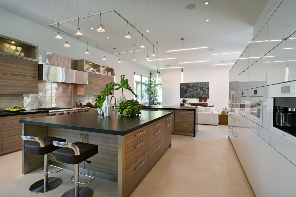 This is an example of a mid-sized contemporary l-shaped kitchen in Miami with a drop-in sink, flat-panel cabinets, beige cabinets, grey splashback, white appliances, with island and beige floor.