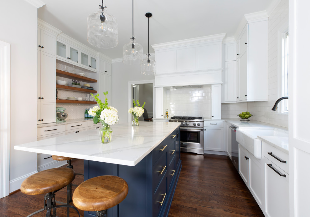 Inspiration for a traditional u-shaped kitchen in Charlotte with a farmhouse sink, shaker cabinets, white cabinets, white splashback, subway tile splashback, stainless steel appliances, dark hardwood floors, with island, brown floor and white benchtop.