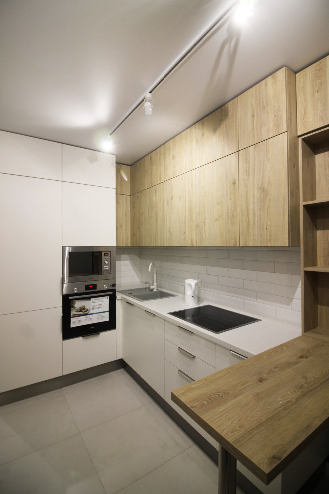 Small scandinavian l-shaped kitchen in Saint Petersburg with a drop-in sink, flat-panel cabinets, white cabinets, solid surface benchtops, white splashback, subway tile splashback, stainless steel appliances, porcelain floors, grey floor and grey benchtop.