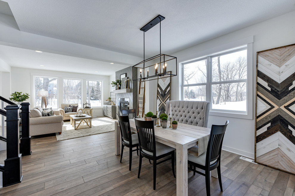This is an example of a mid-sized country dining room in Minneapolis with white walls, laminate floors, a standard fireplace, a tile fireplace surround and grey floor.