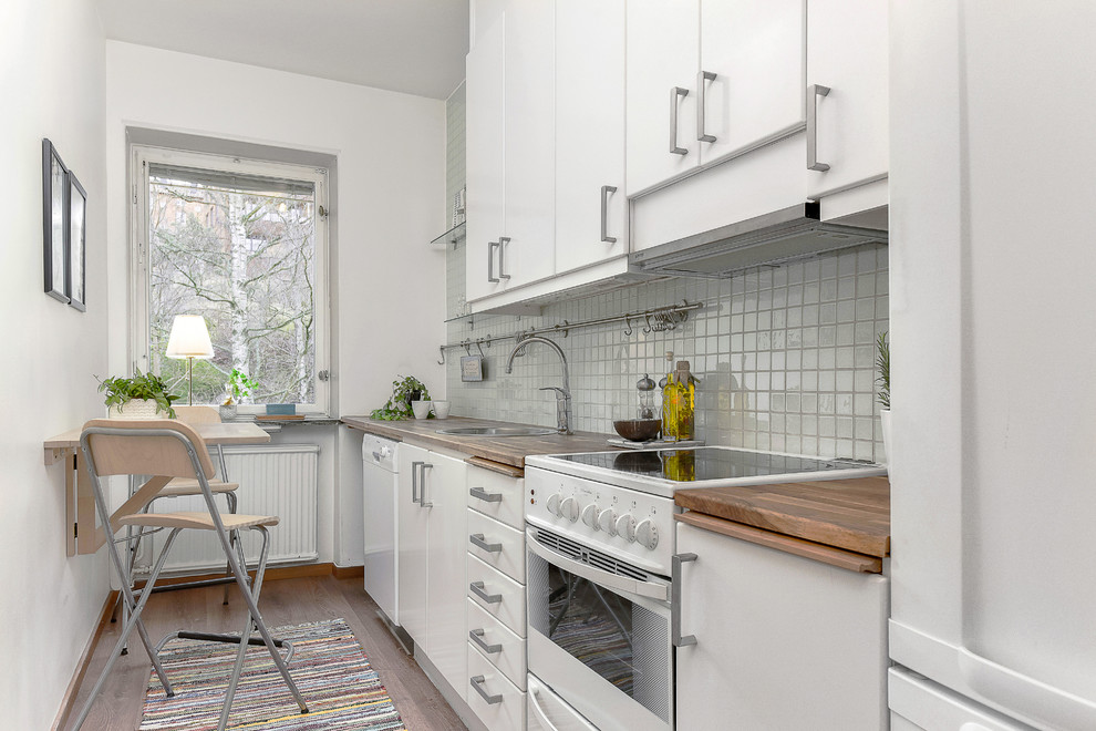 This is an example of a small scandinavian single-wall kitchen in Stockholm with a single-bowl sink, flat-panel cabinets, white cabinets, wood benchtops, white splashback, white appliances, medium hardwood floors, no island and ceramic splashback.
